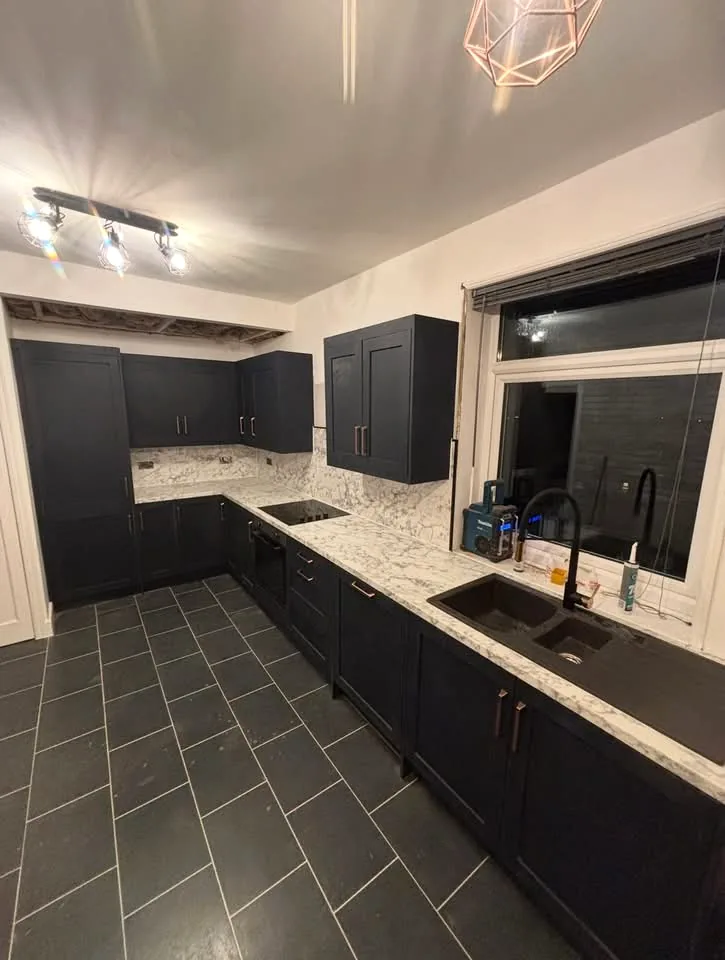 Completed fitted kitchen with dark panelled cabinets and pale patterned worktops